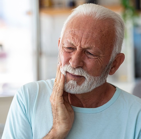 Man in light blue shirt rubbing his jaw in pain