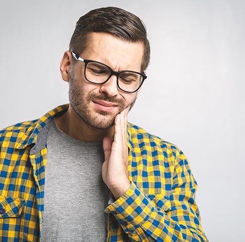 Man with glasses rubbing jaw in pain