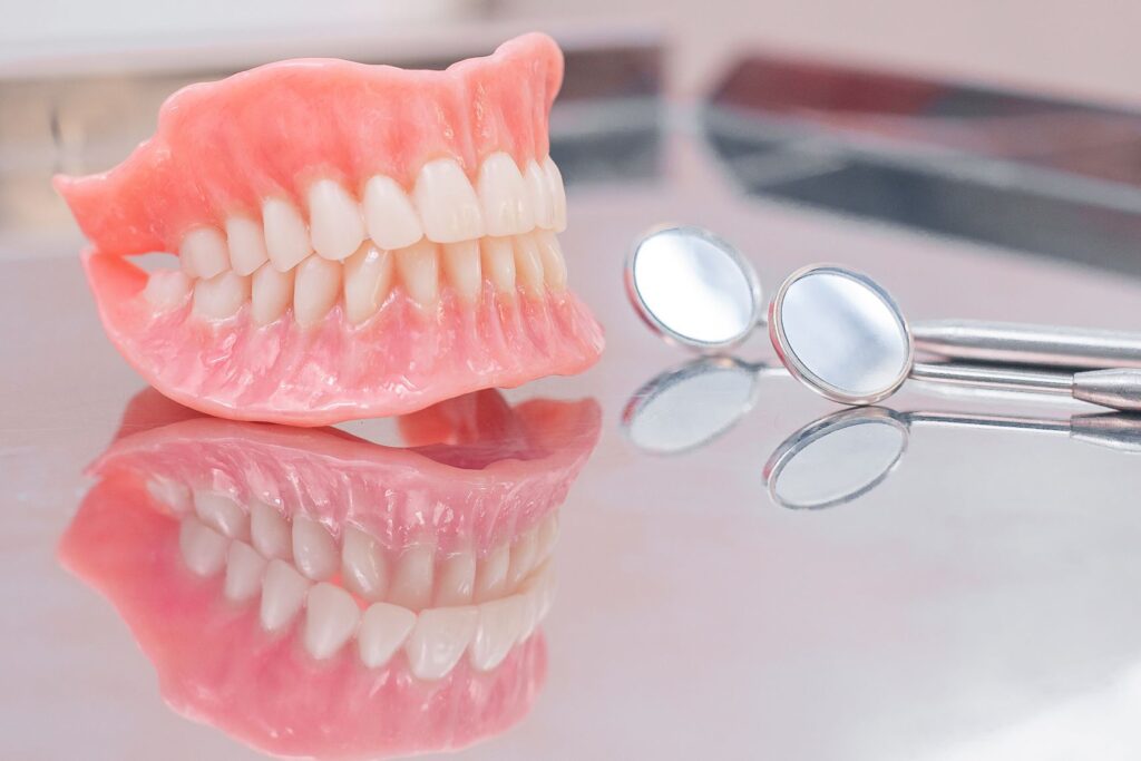 Complete set of dentures on a reflective surface next to dental mirror